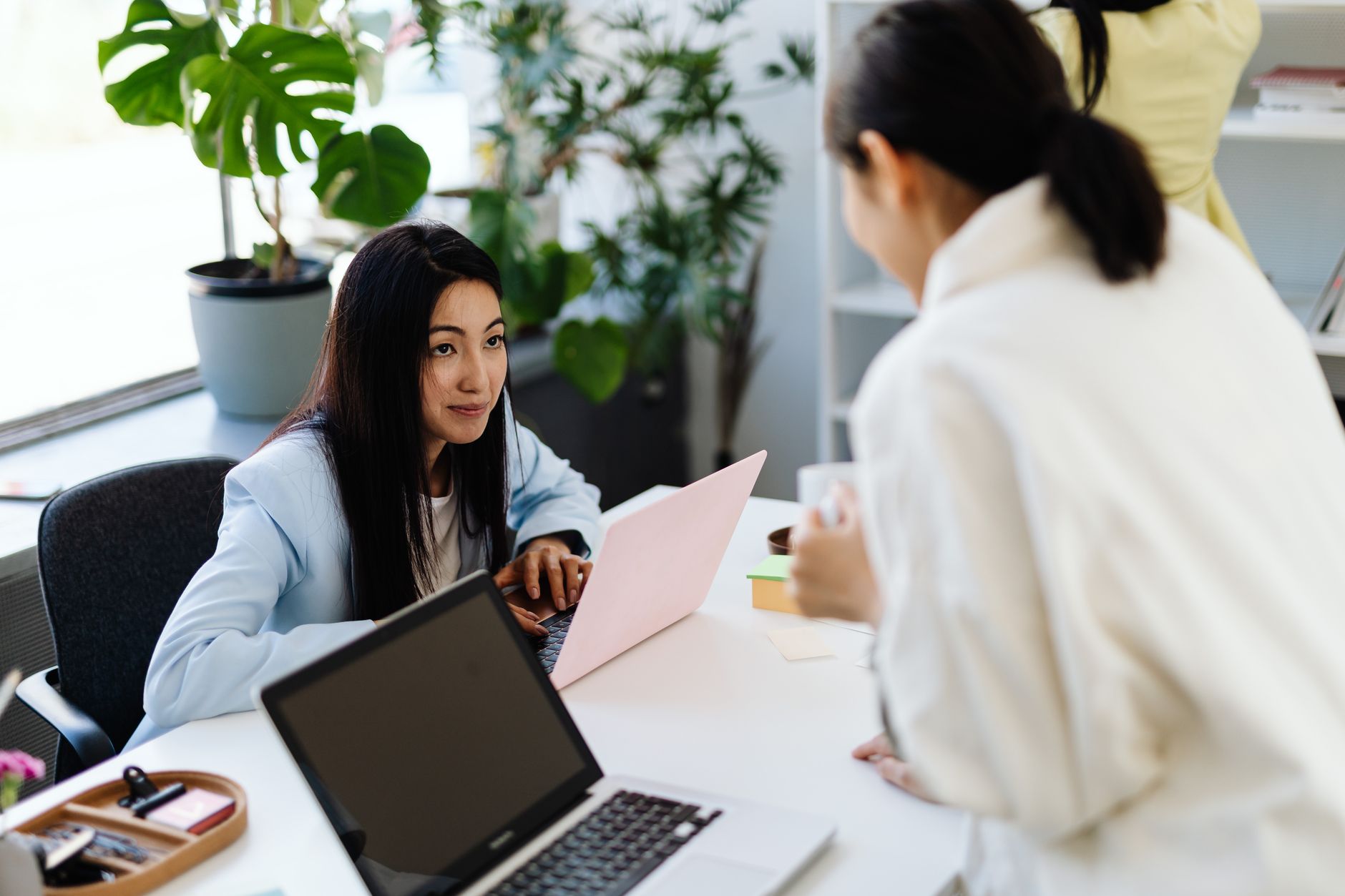 Duas mulheres conversando enquanto trabalham em laptops em um escritório moderno